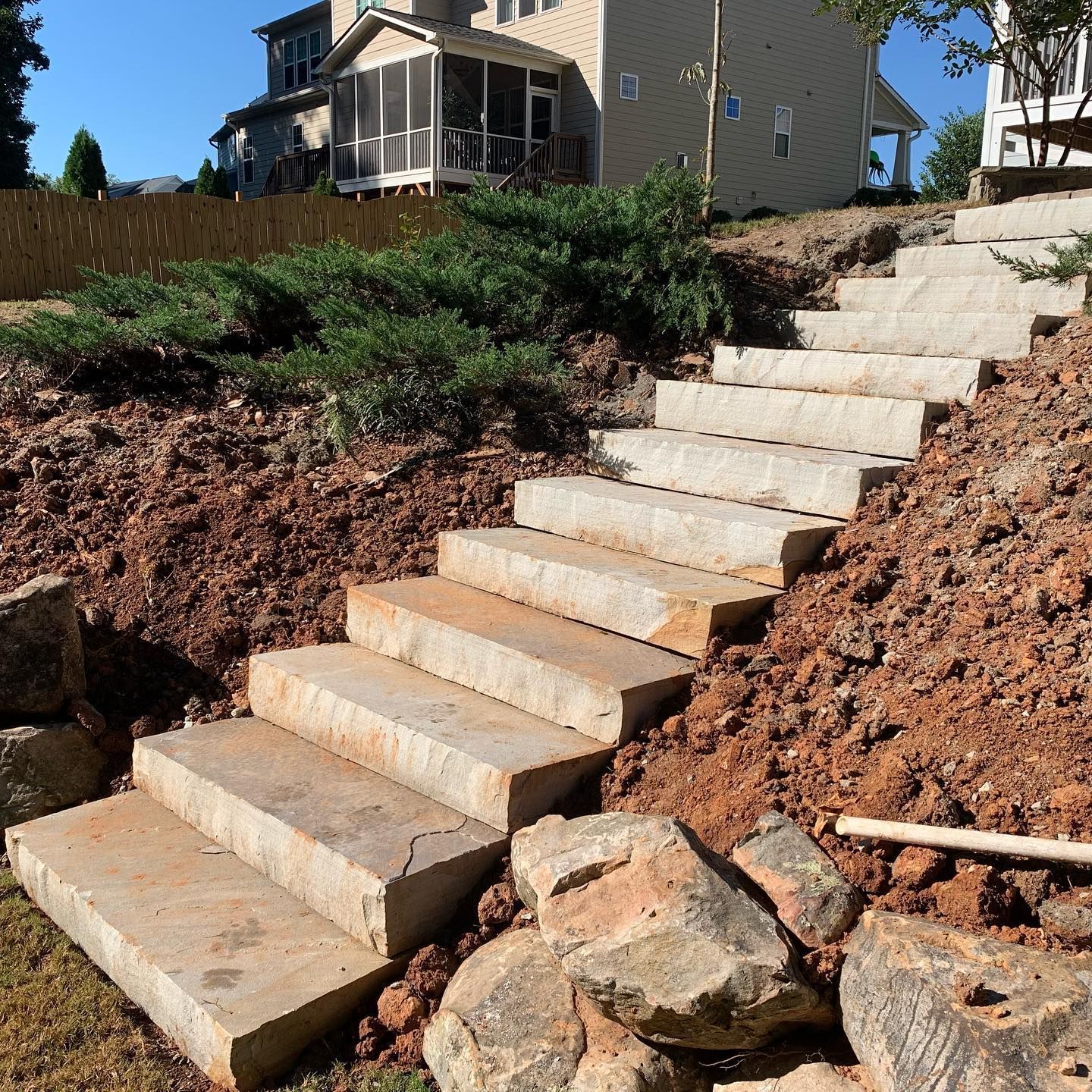Concrete outdoor steps built into a dirt hillside beside a house under construction