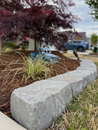 Curved stone landscape border with ornamental grass and a purple-leaf tree in a suburban yard
