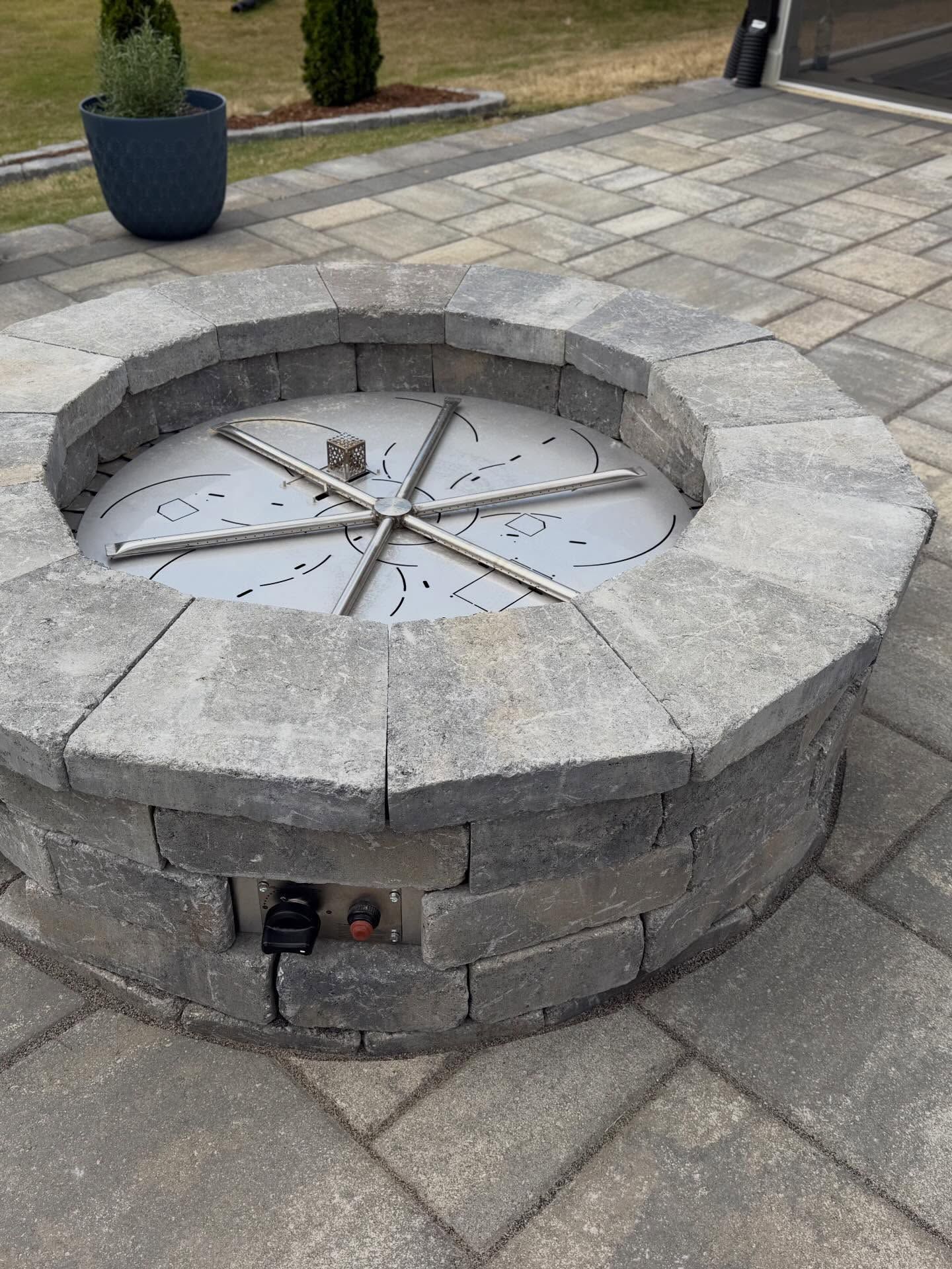 Stone circular fire pit in a paved outdoor courtyard with a metal grate cover