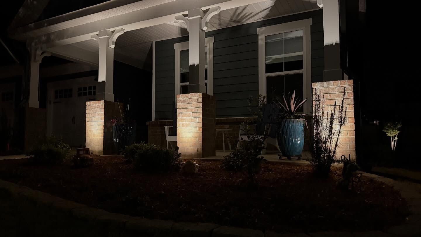 Dimly lit front porch with stone columns, white trim, and potted plants at night