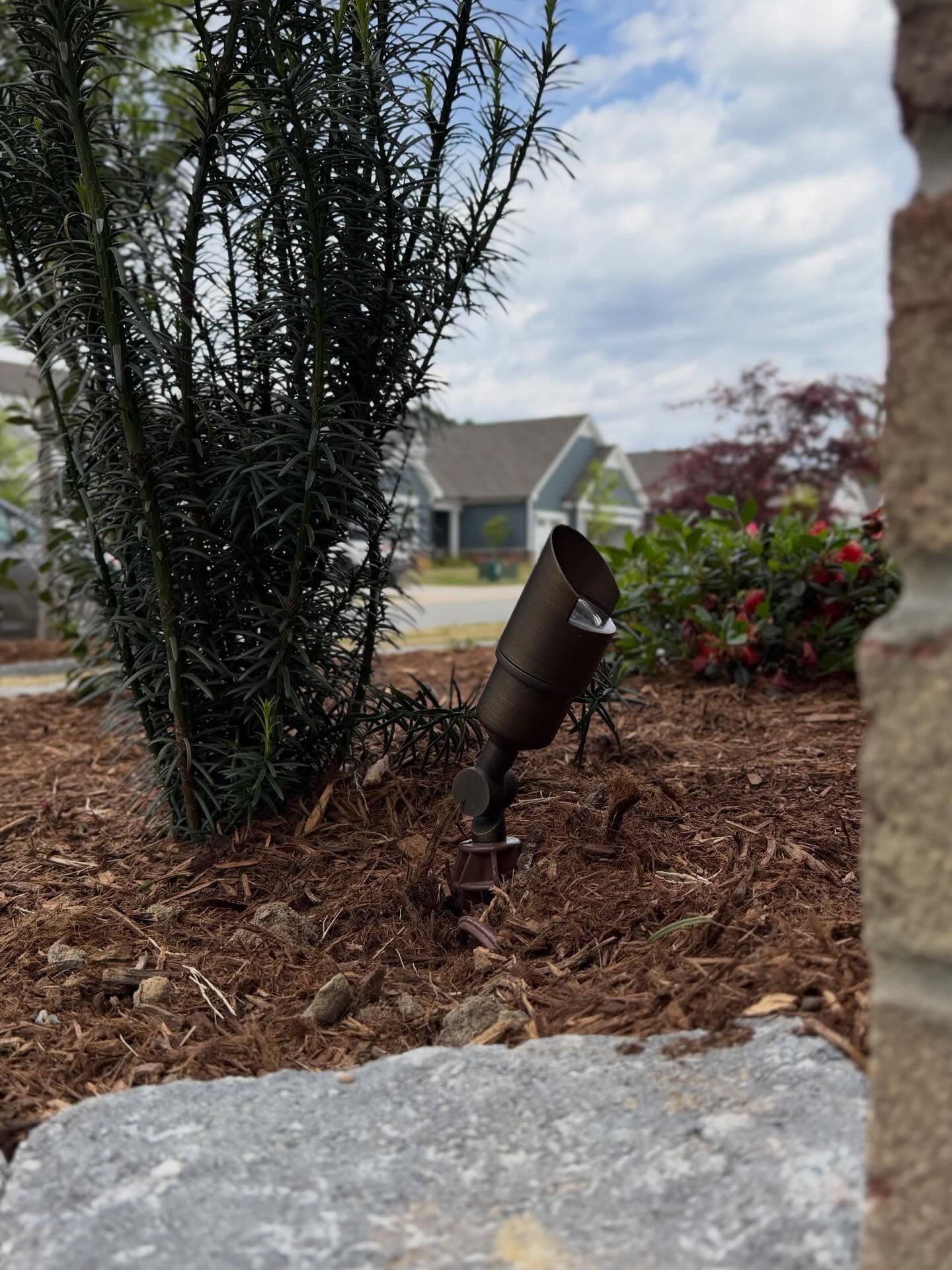 Garden spotlight beside shrubs and mulch, with a house in the background