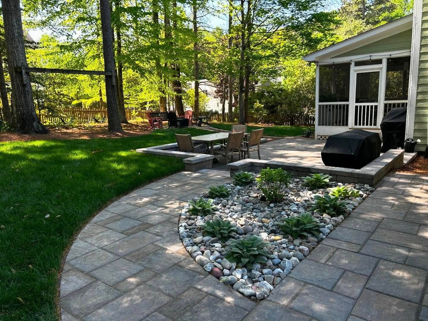 Backyard patio with stone fire pit, paver walkway, lawn, trees, and a screened porch