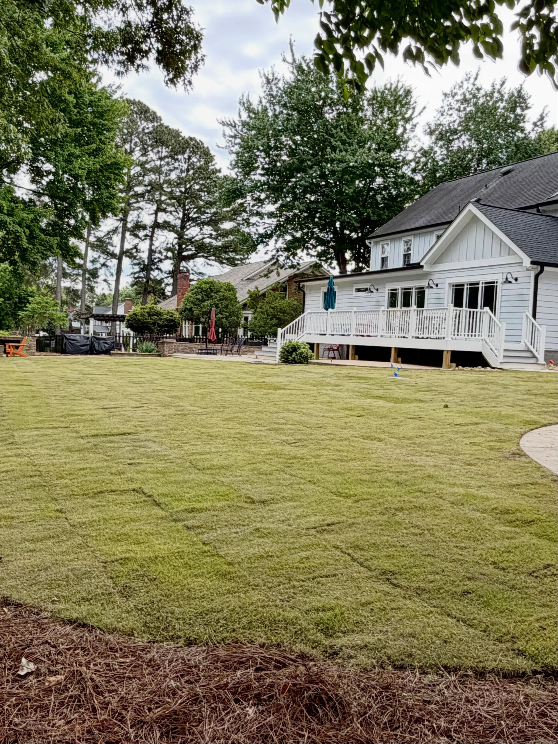 White house with porch beside a wide mowed lawn and trees in a quiet yard
