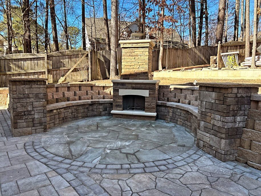Stone outdoor patio with built-in brick seating and fireplace surrounded by trees