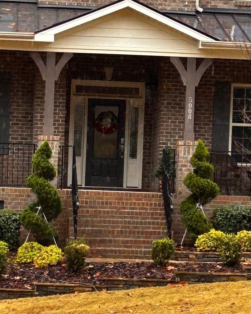 Brick house front porch with white columns, brick steps, and landscaped shrubs