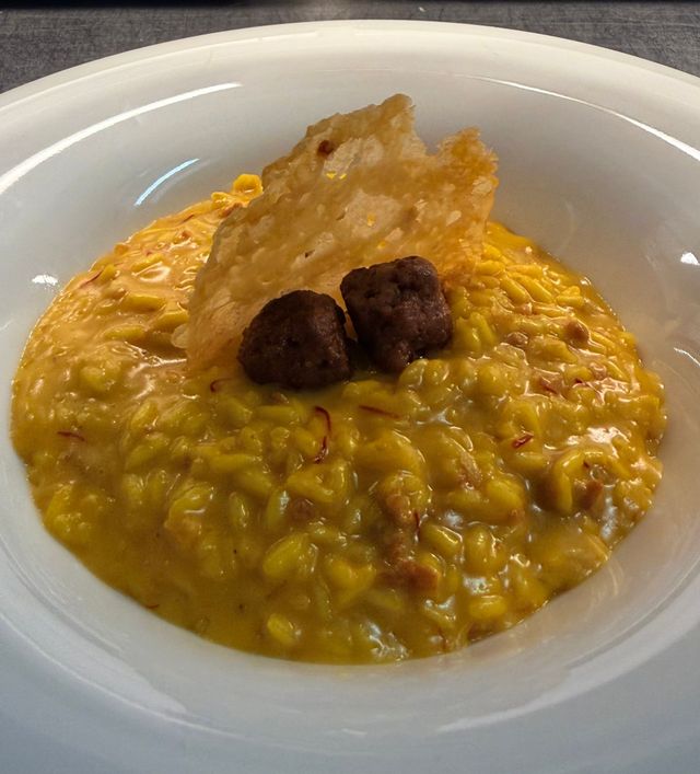 Ciotola di cremoso risotto giallo guarnito con due polpette e una guarnizione croccante