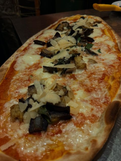 Pizza ovale con formaggio fuso, funghi e basilico su un vassoio scuro