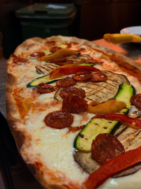 Primo piano di una fetta di pizza vegetariana con zucchine, funghi, peperoni e salame piccante su un piatto.