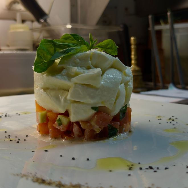 Piatto gourmet a strati guarnito con basilico su un piatto bianco nella cucina di un ristorante.