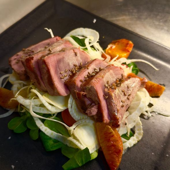 Fettine di bistecca scottate in padella, servite su un piatto nero con verdure, cipolle e salsa di accompagnamento.