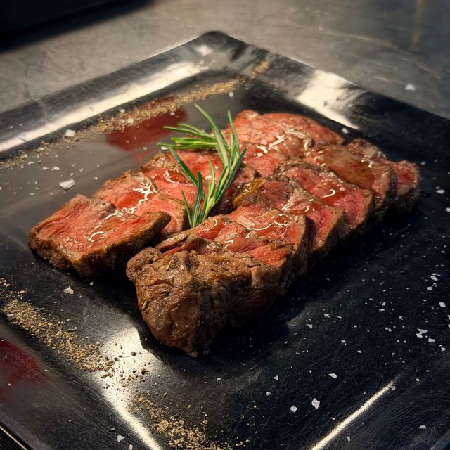 Fettine di bistecca grigliate su un piatto nero, guarnite con rosmarino e una salsa leggera.