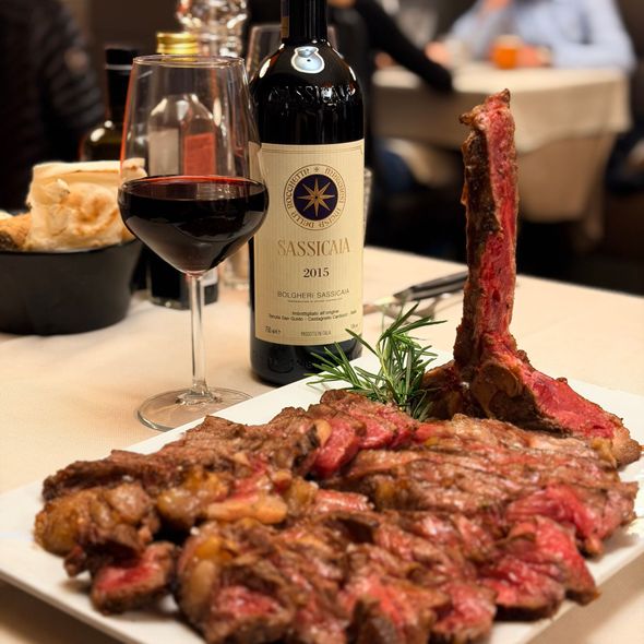 Bottiglia di vino e bicchiere accanto a una bistecca servita su un tavolo di ristorante.