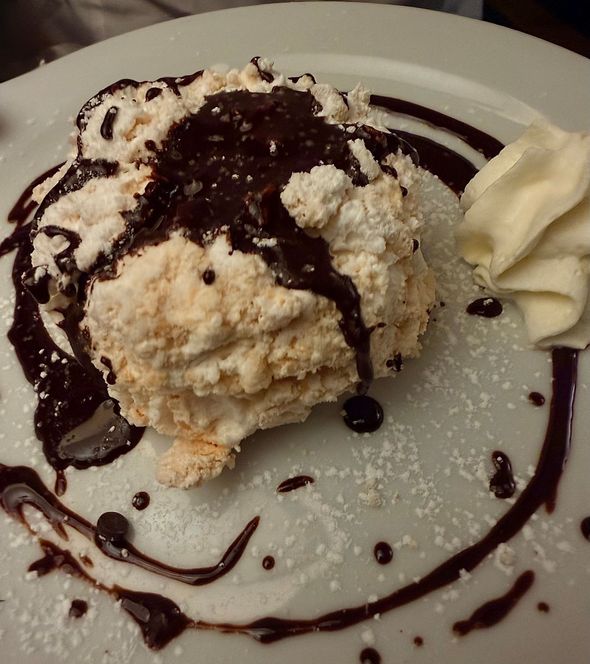 Una pallina di gelato alla vaniglia con una spruzzata di salsa al cioccolato su un piatto bianco, con panna montata a lato.