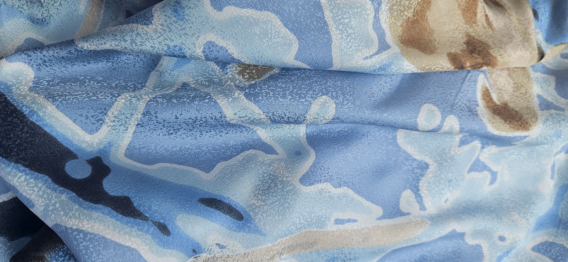 Blauwe bloemenstof met beige en witte patronen, van dichtbij gefotografeerd en gekreukt.