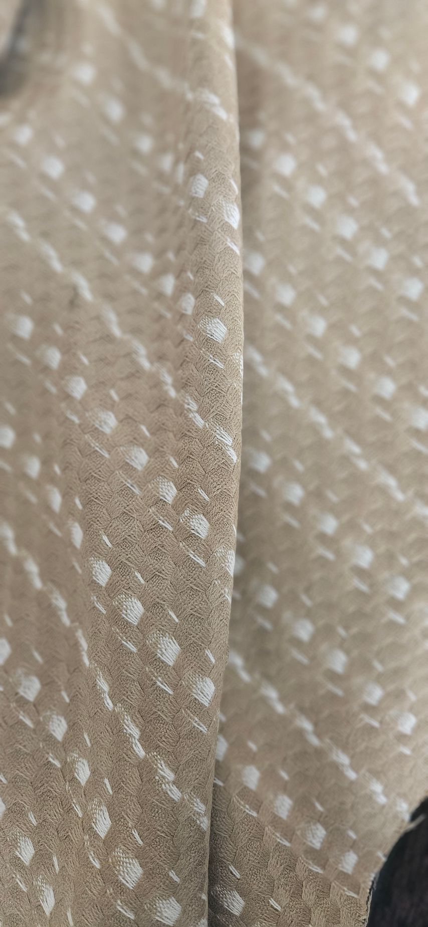 Close-up van beige stof met een wit stippelpatroon en een naad in het midden