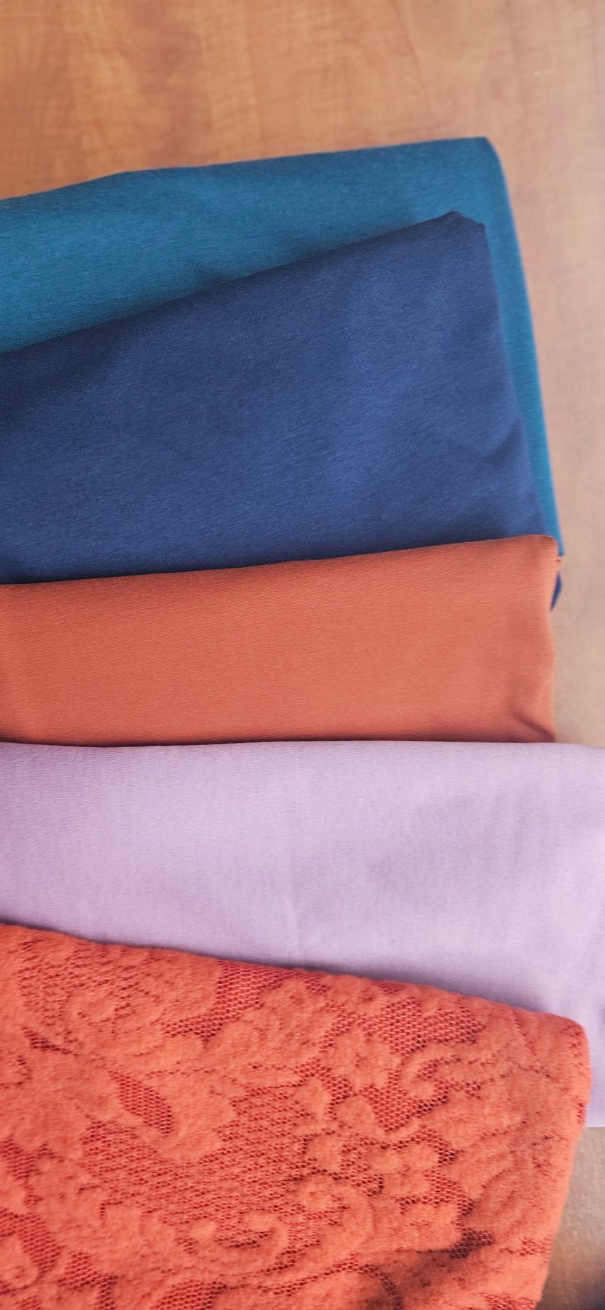 Opgestapelde, gevouwen stoffen in turquoise, marineblauw, koraalrood, lavendel en oranje kant op een houten oppervlak