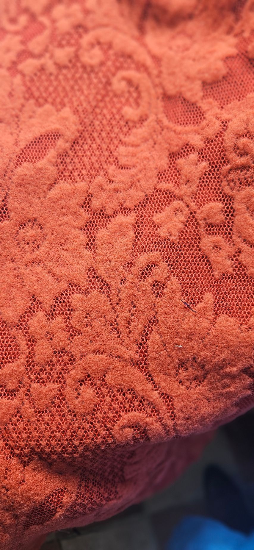 Close-up van oranje stof met structuur, een bloemenpatroon en een donkerblauwe rand