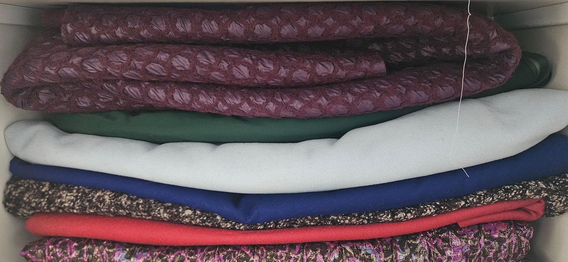 Op elkaar gestapelde, opgevouwen stoffen in paars, groen, wit, blauw, rood en diverse patronen op een plank