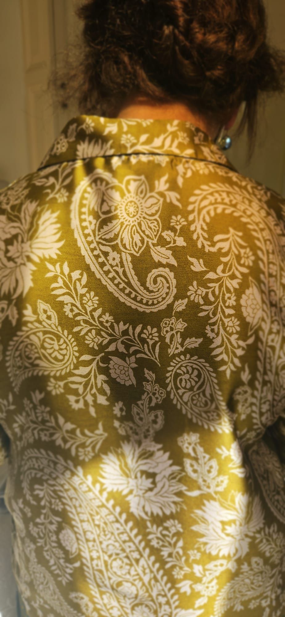 Persoon met een goudkleurig shirt met bloemenpatroon, van achteren gezien in warm licht