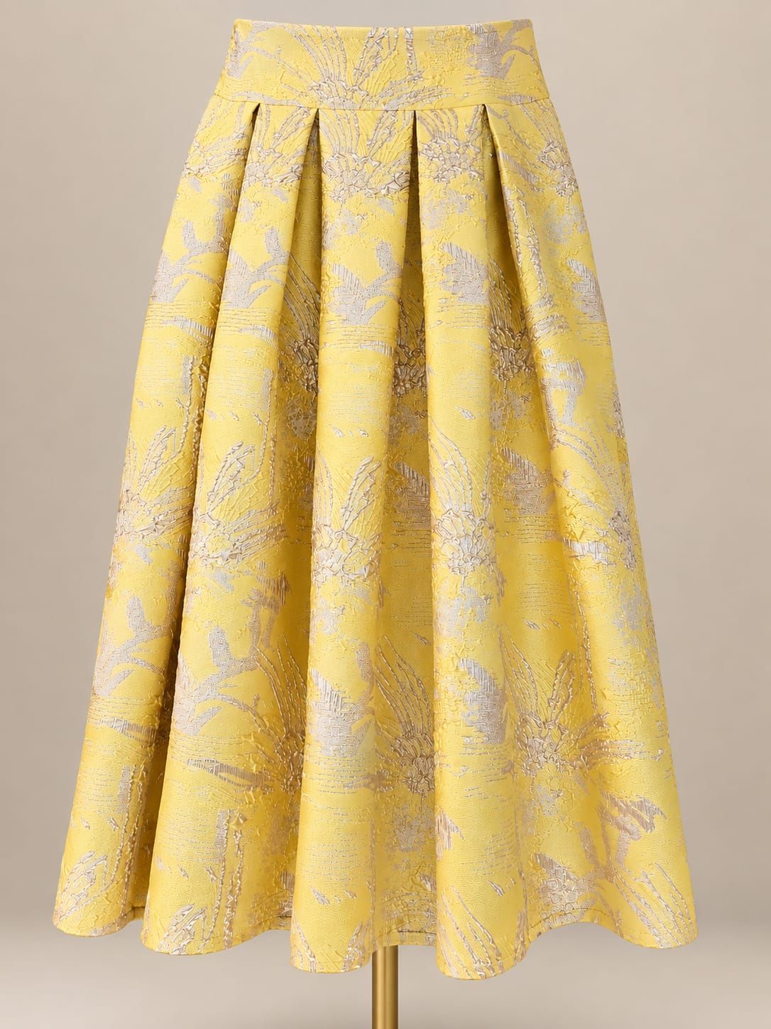 Gele geplooide midirok met een subtiel bloemenpatroon op een beige achtergrond