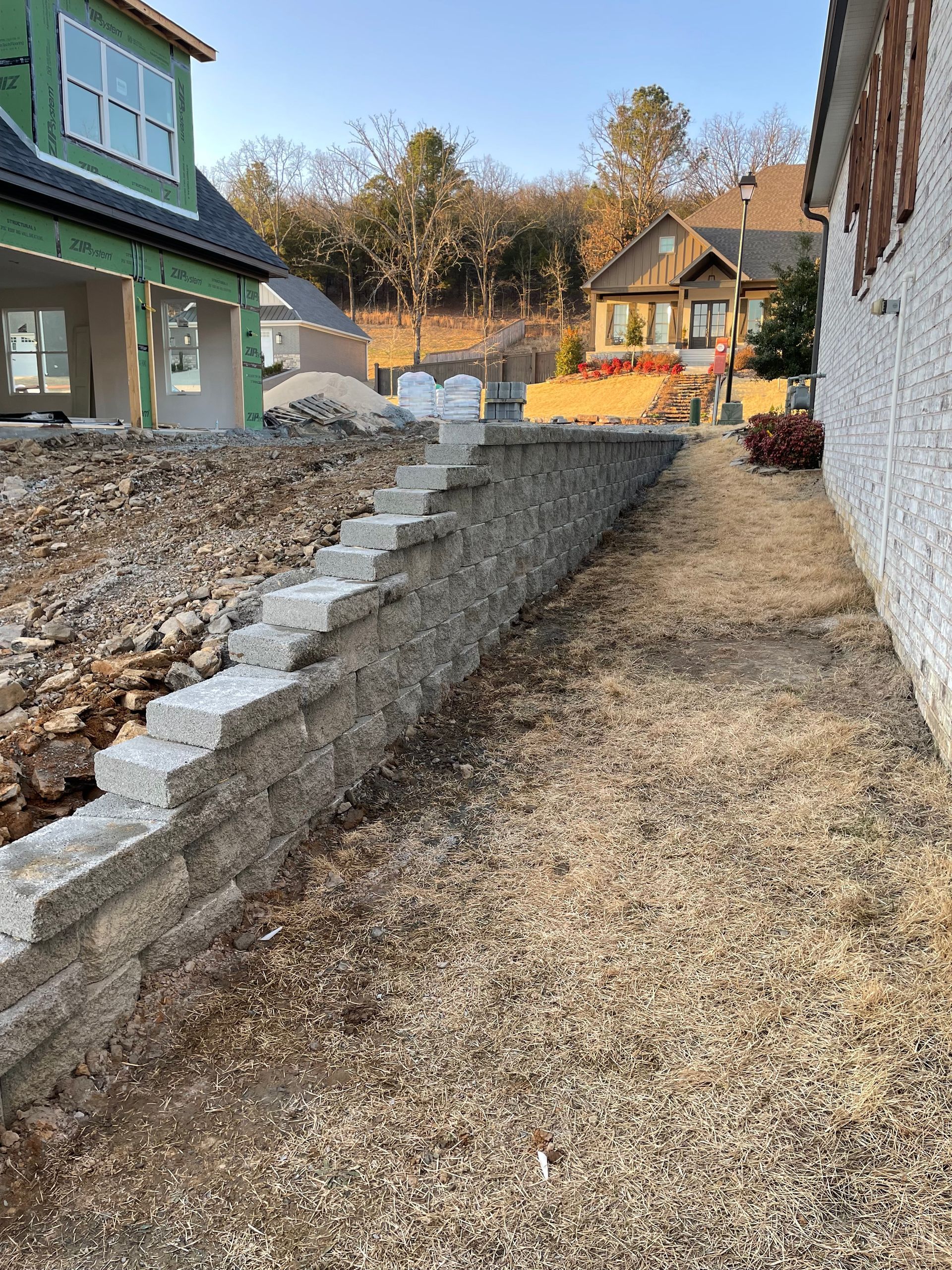 A stone wall is being built next to a house under construction.