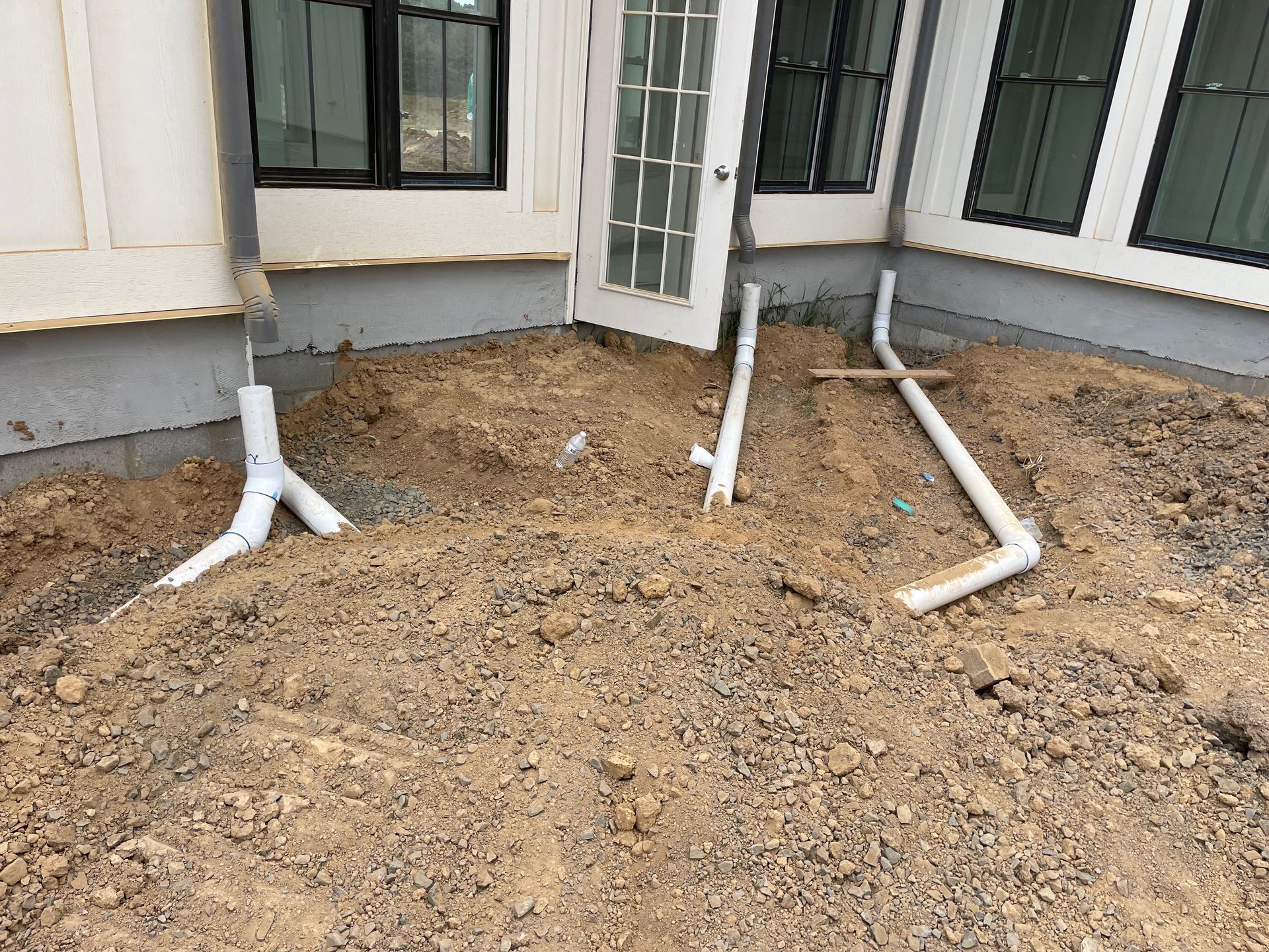 A bunch of pipes are laying in the dirt in front of a house.