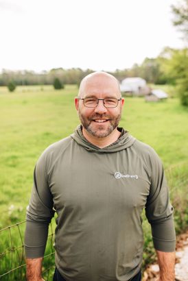 A man wearing glasses and a hoodie is standing in a field.