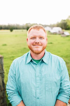 A man with a beard and a green shirt is standing in a field.