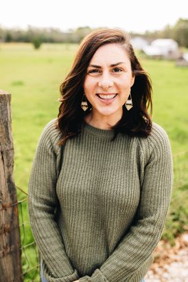 A woman in a green sweater is standing in front of a field.