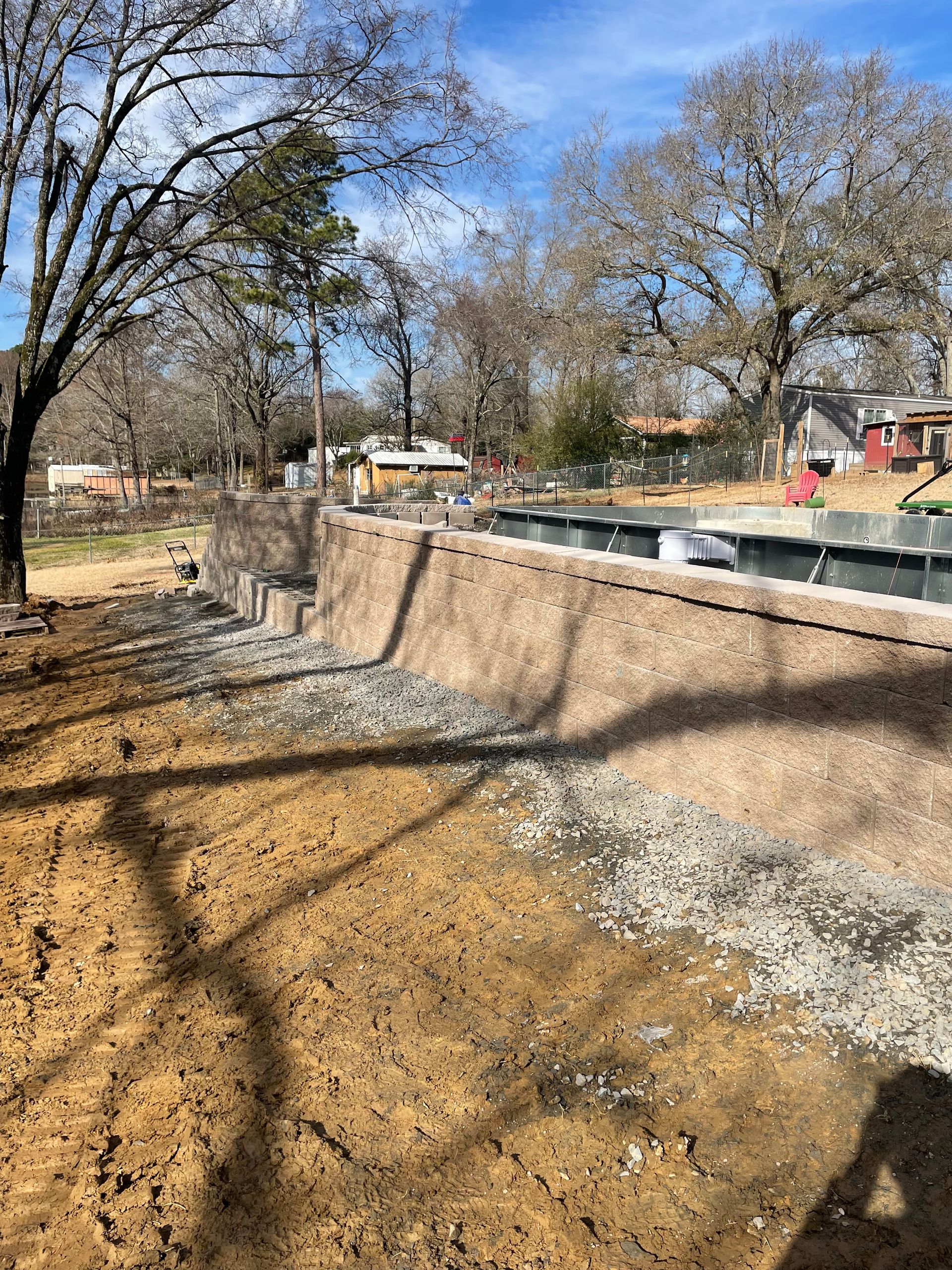 A large concrete wall is being built in a yard with trees in the background.