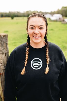 A woman with braids is wearing a black sweater and smiling.