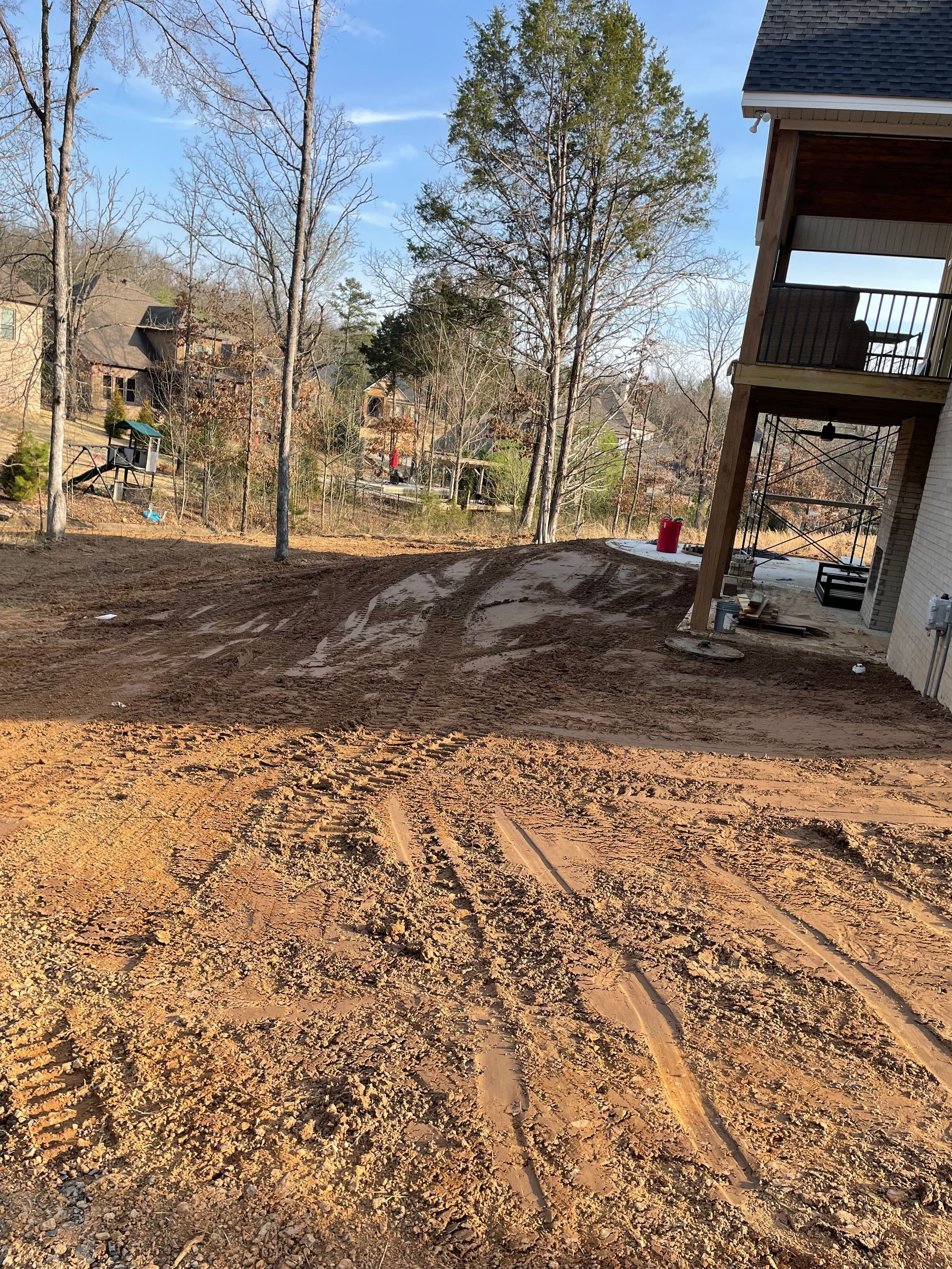 A dirt field with a house in the background and trees in the background.