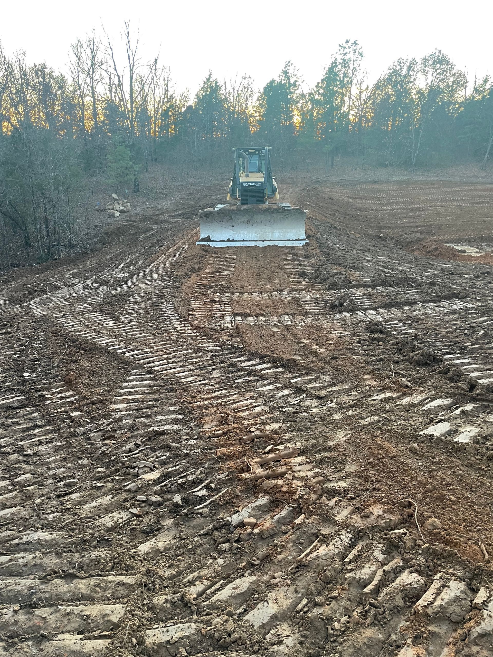A bulldozer is plowing a muddy field with trees in the background.