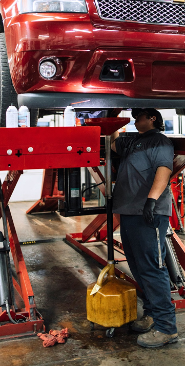 Mechanic working under a lifted red car in an auto shop, using a hydraulic lift. | Keystone Quality Motors