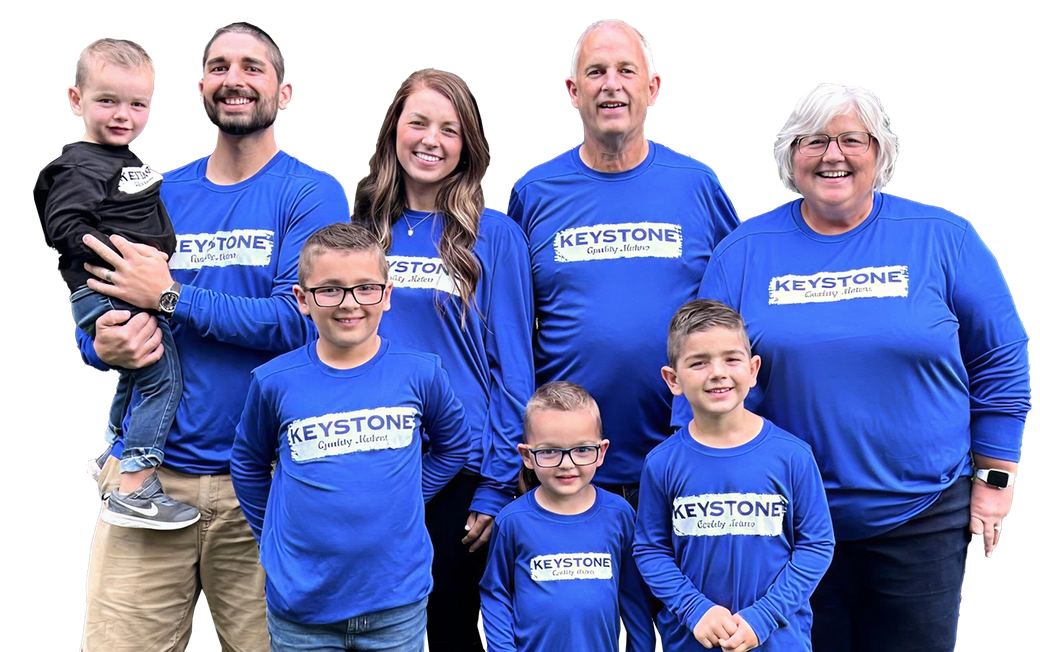 Group of seven people in matching blue shirts posing together against a white background | Keystone Quality Motors