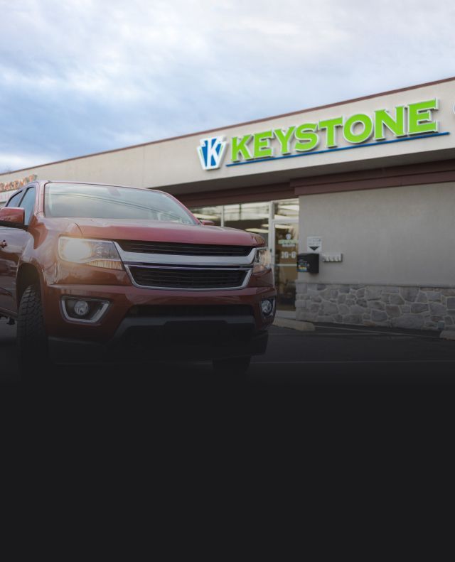 Red Chevrolet SUV parked outside Keystone store under cloudy sky | Keystone Quality Motors