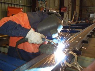 Welder in orange and blue workwear using a welding torch, sparks flying, in a workshop.