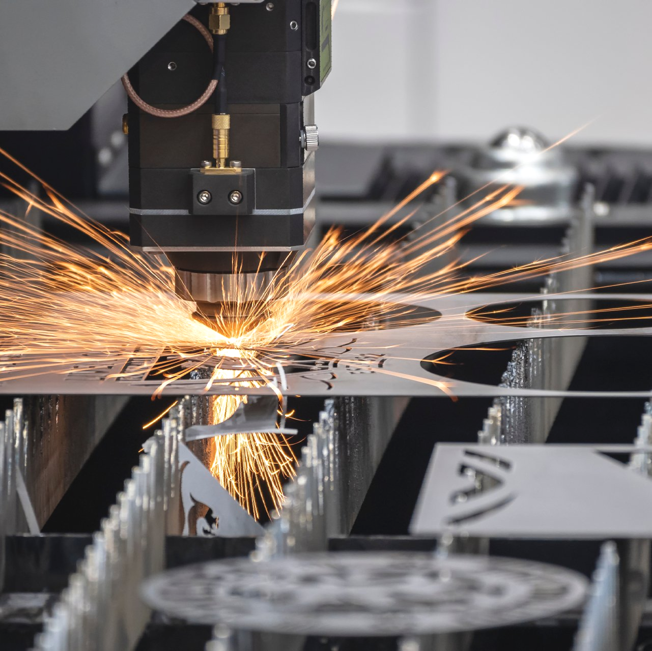 Laser cutter in operation, focused on metal sheet, producing sparks during cutting process.