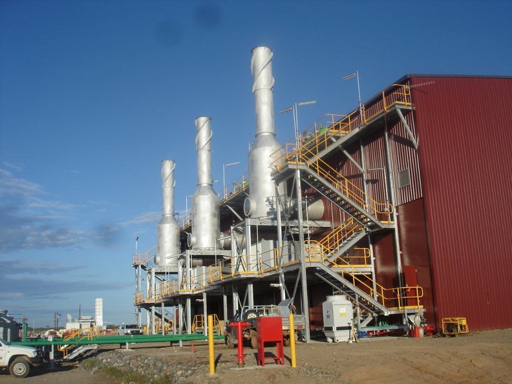 Industrial facility with tall silver stacks, metal platforms, and a red building against a blue sky.