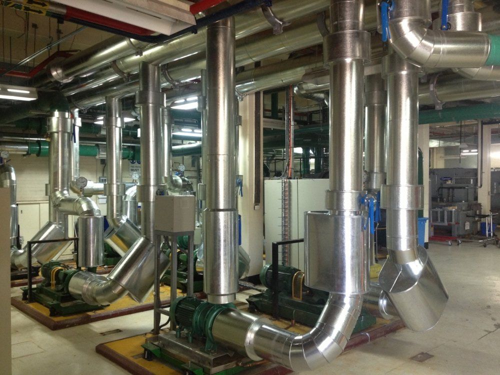 Pipes and pumps in an industrial setting. Silver pipes curve down to green pumps, on platforms in a utility room.