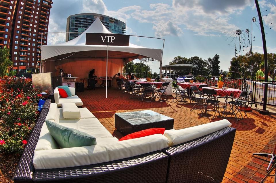 VIP outdoor lounge with white sectional seating, red accents, tables, and umbrellas on a sunny patio