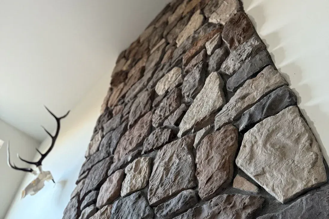A tall, stone-tiled fireplace wall in a modern room with an elk skull mount hanging on the adjacent white wall.