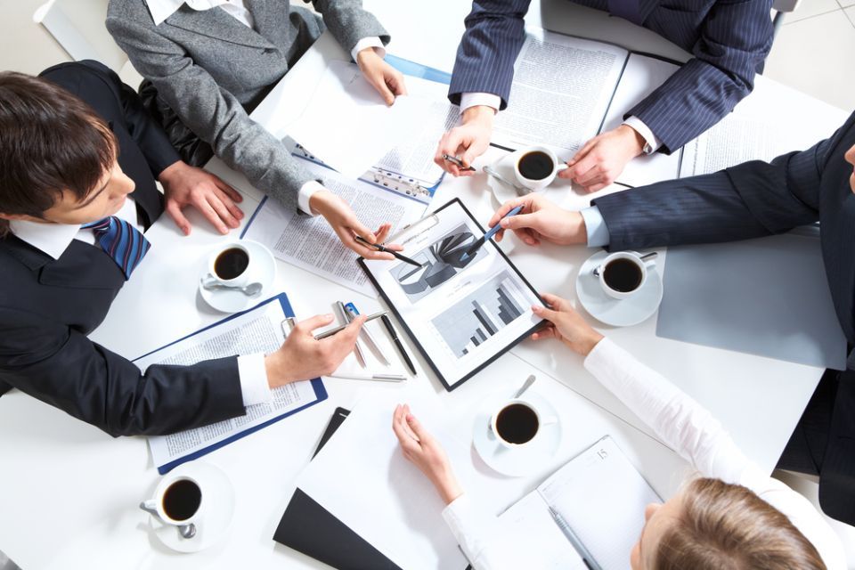Business team meeting around a table with charts, laptops, coffee cups, and documents