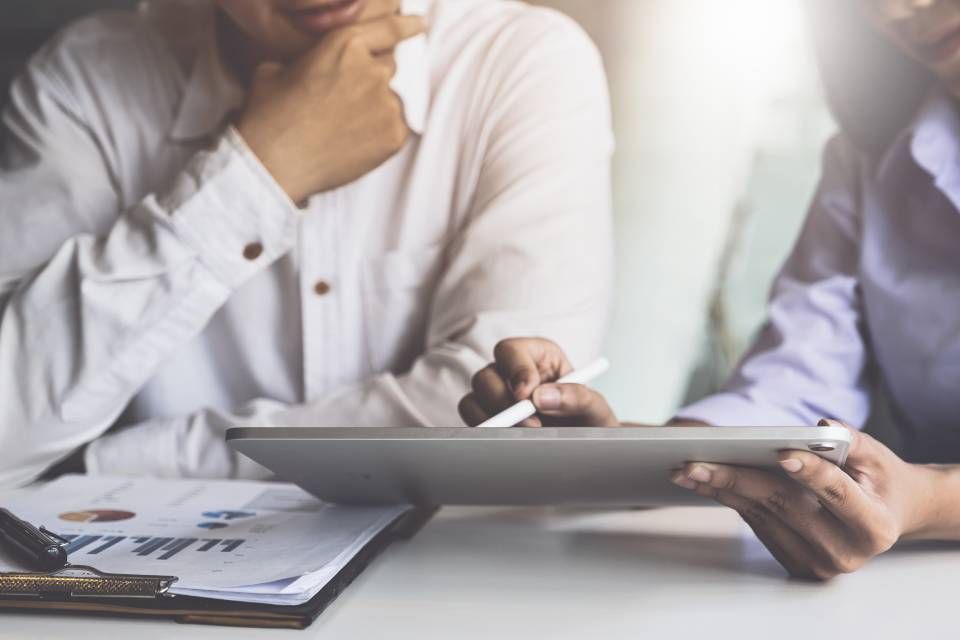 Two people reviewing financial documents and a tablet at a desk