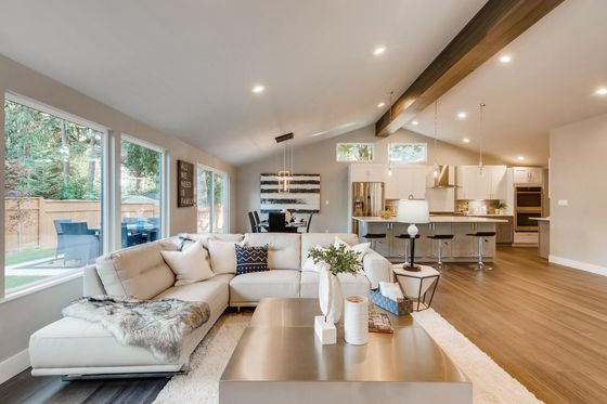 Bright open-concept living room with white sofa, large windows, wooden beams, and modern kitchen beyond