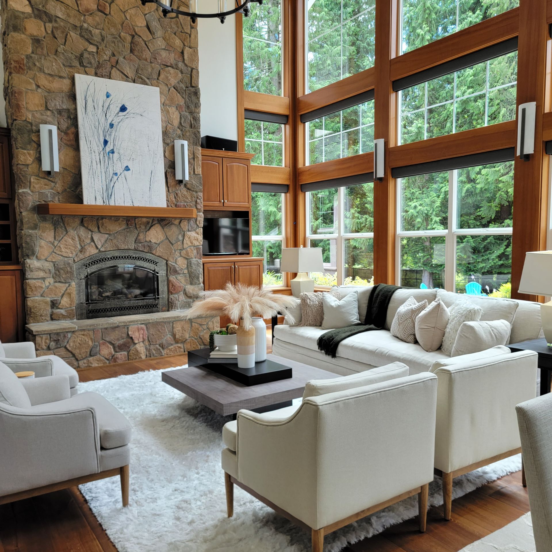 Bright modern living room with stone fireplace, large windows, white sofas, and wood accents