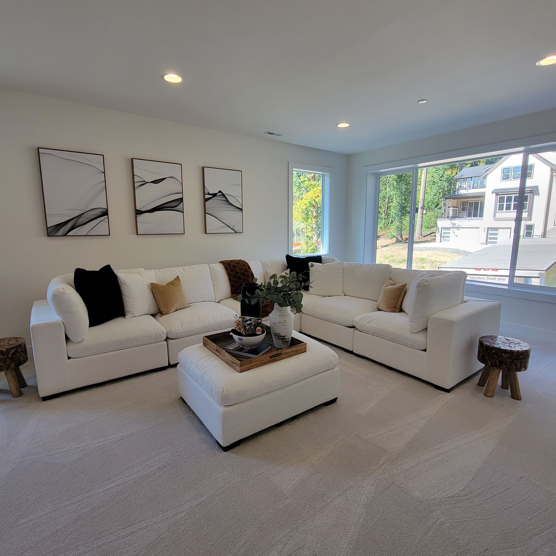 Bright modern living room with white sofas, coffee table, wall art, and large windows