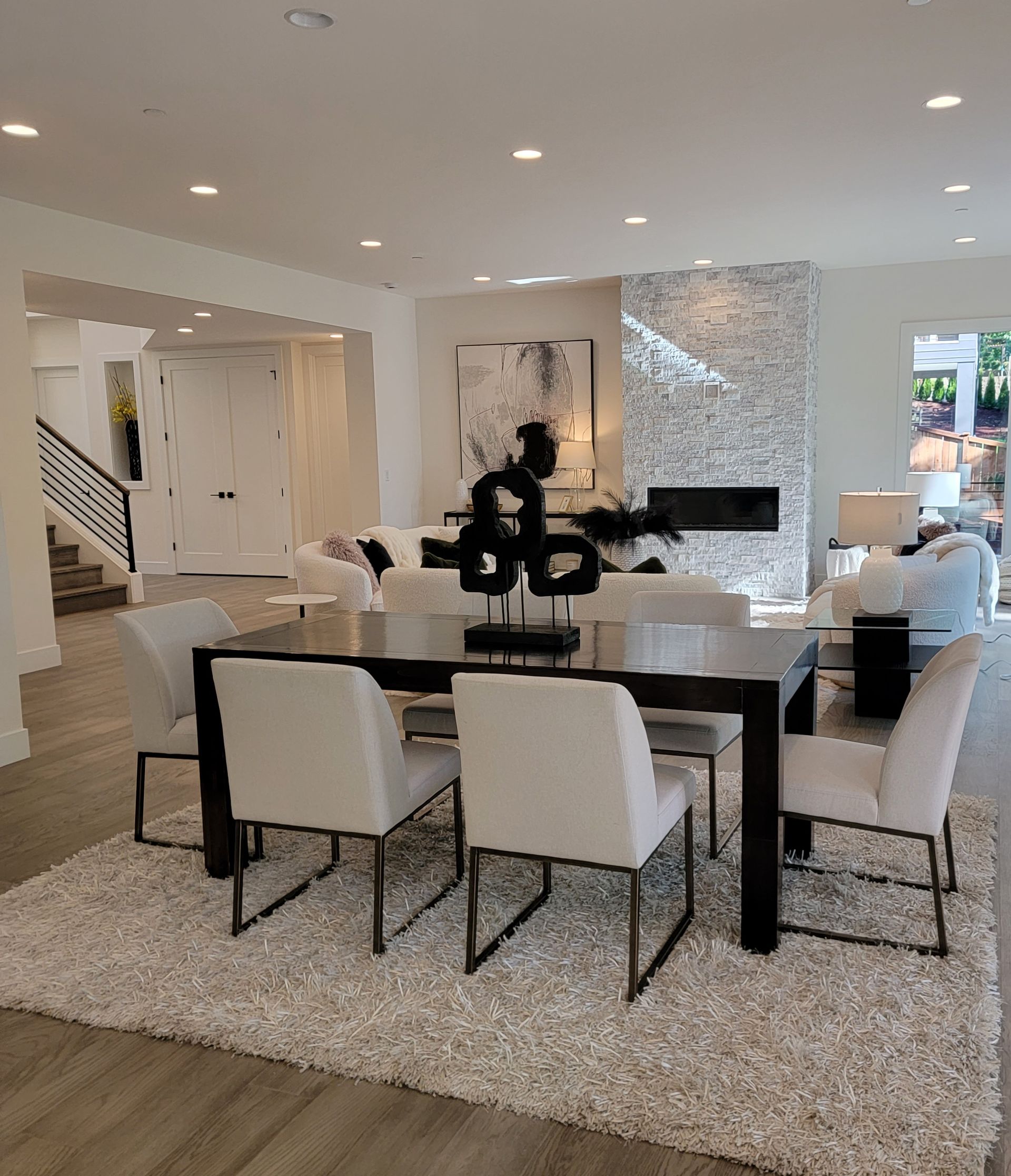 Modern dining room with white chairs, black table, chandelier, and a stone fireplace wall