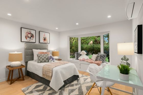 Bright modern bedroom with a bed, lounge chair by the window, and soft neutral decor