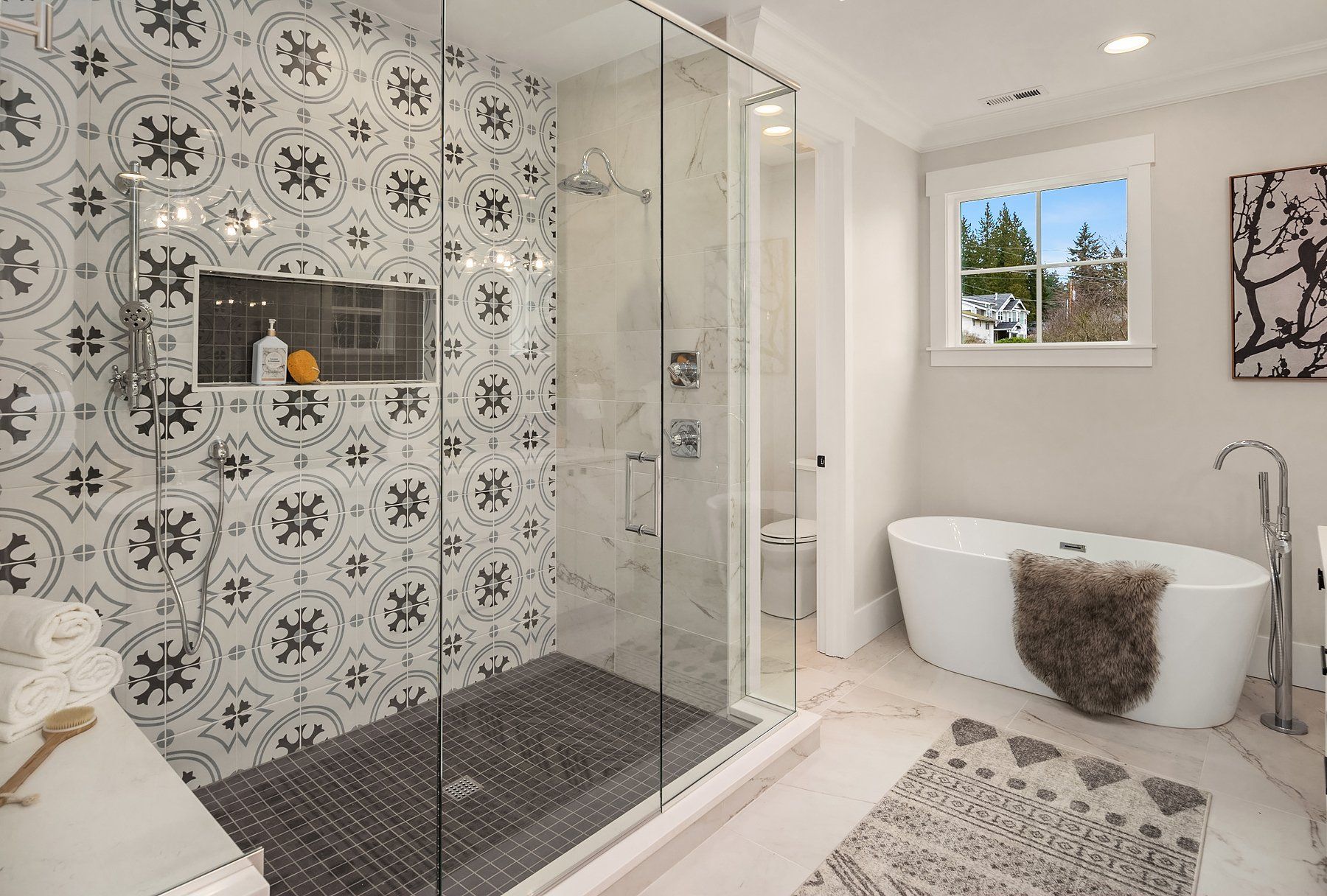 Modern bathroom with patterned tile shower, freestanding tub, and window above a rug
